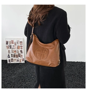 Close-up of a large brown leather hobo bag with an embossed round logo on a black blazer