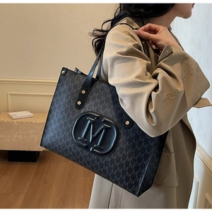 Detail of a black tote bag with embossed M logo and monogram pattern on a shoulder strap