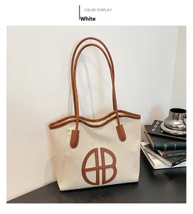 Detail of cream woven tote bag with brown leather straps and large HB logo on a desk