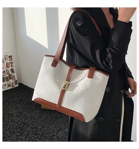 Detail of white woven tote bag with brown leather trim and golden metal clasp closure