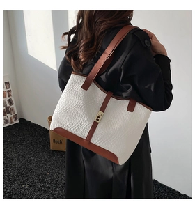 Detail of white woven tote bag with brown leather trim and metallic lock buckle