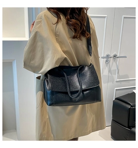 Detailed shot of large black tote with shimmering texture worn with a beige trench coat
