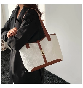 Detail of white embossed leather tote bag with brown trim and gold lock worn by model