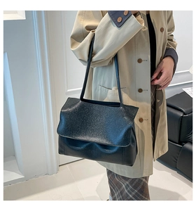 Detail of black large capacity shoulder bag with textured flap on a model in trench coat