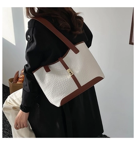 On-shoulder view of a large contrast-color woven tote bag with brown leather trim