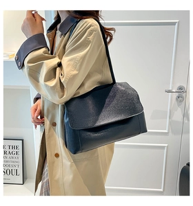 Close-up of minimalist black leather shoulder bag with flap closure on a model