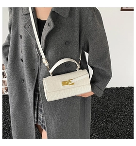 Detailed shot of a white woven shoulder bag with gold hardware worn by a model in a minimalist room