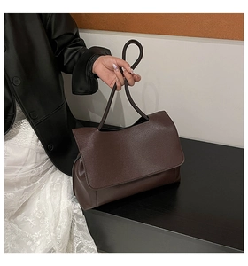 Macro shot of dark brown faux leather shoulder bag with sleek handle and foldover flap