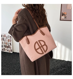 Side view of pink woven tote bag with brown straps worn by a model in a minimalist setting