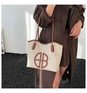Chic beige woven tote bag with brown leather handles worn by model in a stylish setting