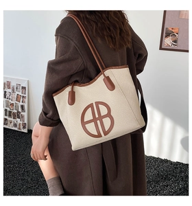 Detail of beige woven tote bag with brown leather trim and circular AB logo patch