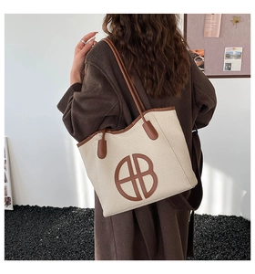 Detail of a beige woven tote bag with brown leather trim worn by a model in a modern setting