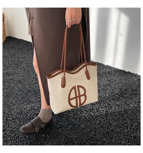 Detail of a large beige woven tote bag with brown leather trim and circular B logo