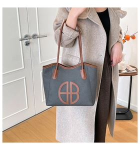 Close-up of woven bucket tote bag with brown leather handles and HB logo patch