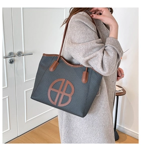 Close-up of grey woven tote bag featuring brown leather trim and large AB logo patch