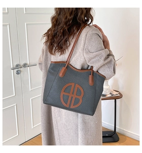 Detail of large woven grey tote bag with brown leather straps and cutout logo shown on shoulder