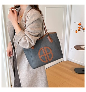 Detail view of a large woven tote bag with leather trim and round logo on the model shoulder