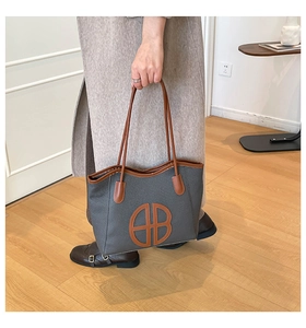 Close-up of a large grey fabric tote bag with brown leather handles and logo patch