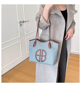 Close-up of light blue woven tote bag featuring brown leather trim and circular AB logo