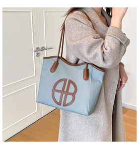 Detail of light blue woven tote bag with brown leather handles and AB logo patch