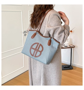 Detail of blue woven tote bag with brown leather logo and slim shoulder straps