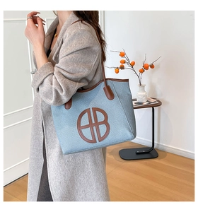 Detail of blue woven tote bag with brown leather trim and circular HB logo patch