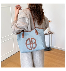 Dettaglio della borsa tote intrecciata blu con finiture in pelle marrone e logo AB