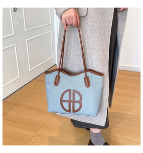Detail of light blue woven tote bag featuring dark brown leather logo and handle