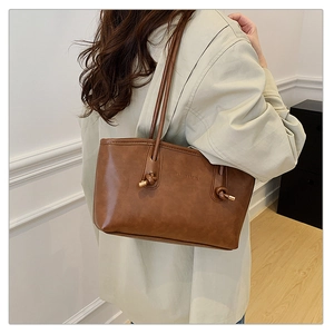 Close-up of brown leather tote bag featuring a knotted strap design and fashion text detail