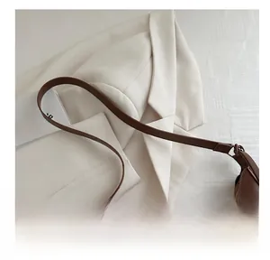Gros plan sur la texture du cuir brun et les détails métalliques du sac demi-lune
