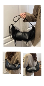 Detail of black leather hobo bag featuring a gold metal logo and side tassel accents
