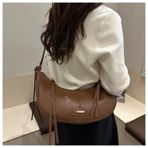 Detail view of dark brown crescent bag with gold plate and long tassels on shoulder strap