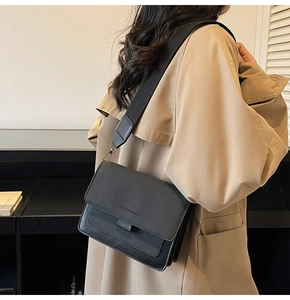 Detail of a black crossbody bag with wide fabric strap and fashion text on the flap