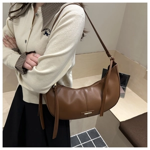 Detail view of brown leather crescent bag featuring long tassel and gold metal hardware