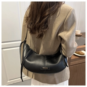 Détail d'un sac demi-lune noir en cuir mat avec une plaque métallique et fermeture éclair