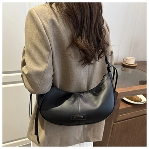 Detail of minimalist black dumpling bag with metal bar and adjustable shoulder strap