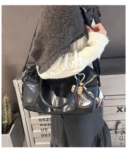Close-up of black leather tote bag with heart pendant worn by model in casual style
