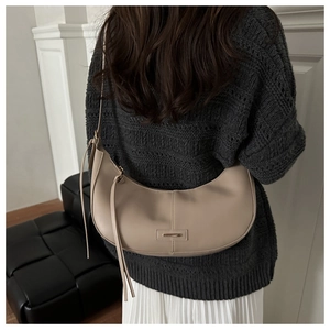 Close-up of a stylish khaki half-moon shoulder bag worn by a model in a minimalist room
