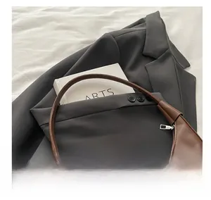 Detailed view of brown leather crescent bag with stitching on a dark gray suit