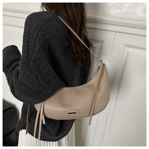 Detail view of beige crescent bag featuring black trim and long fringe tassel accents