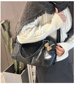 Detail of black faux leather tote bag with heart charm and leopard bow on model