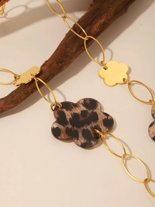 Macro detail of gold-plated chain necklace with leopard print flower charms on wood