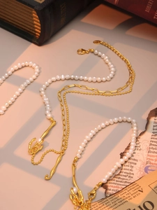 Dettaglio collana multistrato con perle barocche, catene dorate e ciondolo artistico