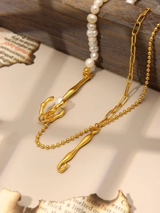 Dettaglio di pendenti in metallo dorato irregolari e perle barocche su collana asimmetrica