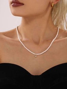 Dettaglio di una collana di perle con ciondolo a cuore e orecchini d'oro indossati