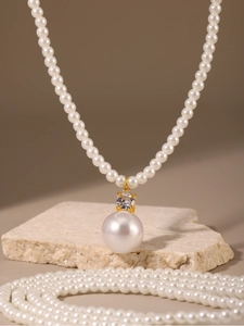 Détail d'un pendentif en perle blanche et zircon sur un collier doré avec des perles