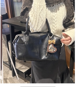 Close-up of black Boston bag with leopard heart charm held by a woman in a cafe