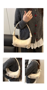 Detail view of cream crescent bag with decorative silver buckles and vegan leather texture