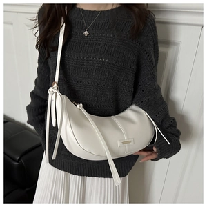 Close-up of a white crescent moon shoulder bag with decorative straps and smooth leather texture