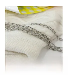 Detailed close-up of a glossy silver metal chain link on a white knitted fabric